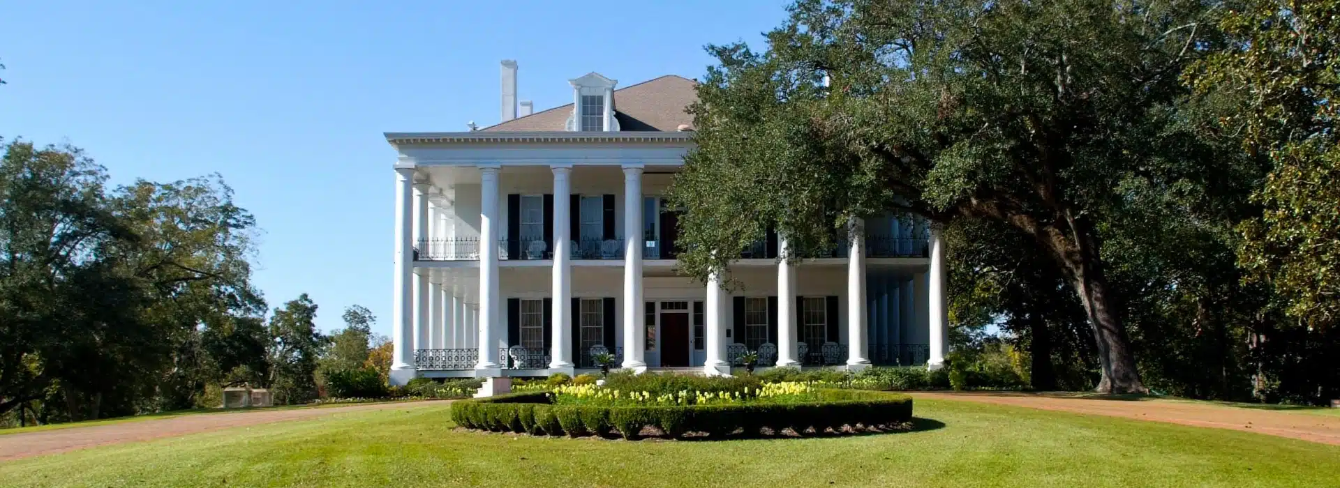 Historic plantation house with columns and manicured lawn.